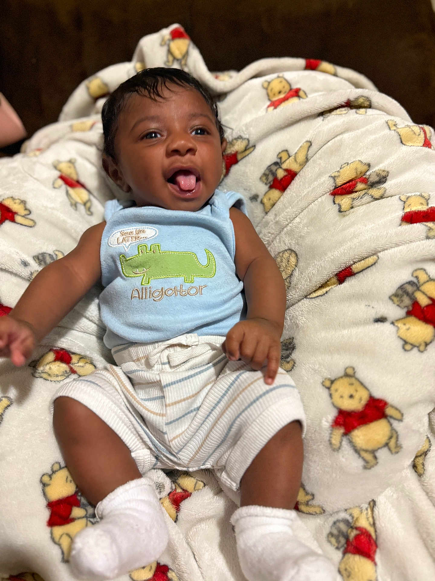 Christopher is registered to the contest to win money with this photo: baby, child, infant, smiling, tongue_out, blue_clothing, striped_shorts, white_socks, blanket, winnie_the_pooh, plush_blanket, happy, cute, lying_down, indoors, closeup, soft_texture, playful, young_child, cozy
