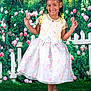 child, girl, smiling, posing, dress, floral, lace, bolero, peace_sign, braided_hair, beads, garden, flowers, greenery, white_picket_fence, grass, footwear, sandals, portrait, happy