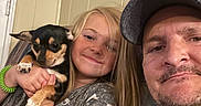 Polly Pocket is registered to the contest to win money with this photo: puppy, dog, girl, man, family, selfie, portrait, smiling, hugging, pet, black_and_tan, small_dog, indoors, home, wall, hat, beard, long_hair, child, companion