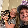 puppy, dog, girl, man, family, selfie, portrait, smiling, hugging, pet, black_and_tan, small_dog, indoors, home, wall, hat, beard, long_hair, child, companion