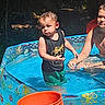 child, pool, water, outdoor, summer, sunlight, orange_bucket, greens, playing, splash, tank_top, shorts, nature, fun, kids, sunny_day, backyard, water_toy, happy, sibling