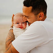 Raphaëlle participe au concours pour gagner de l'argent avec cette photo : baby, man, hug, tattoo, beach, smile, affection, love, outdoor, portrait, skin, white_shirt, closeup, father, child, person, casual_clothing, emotion, head, family