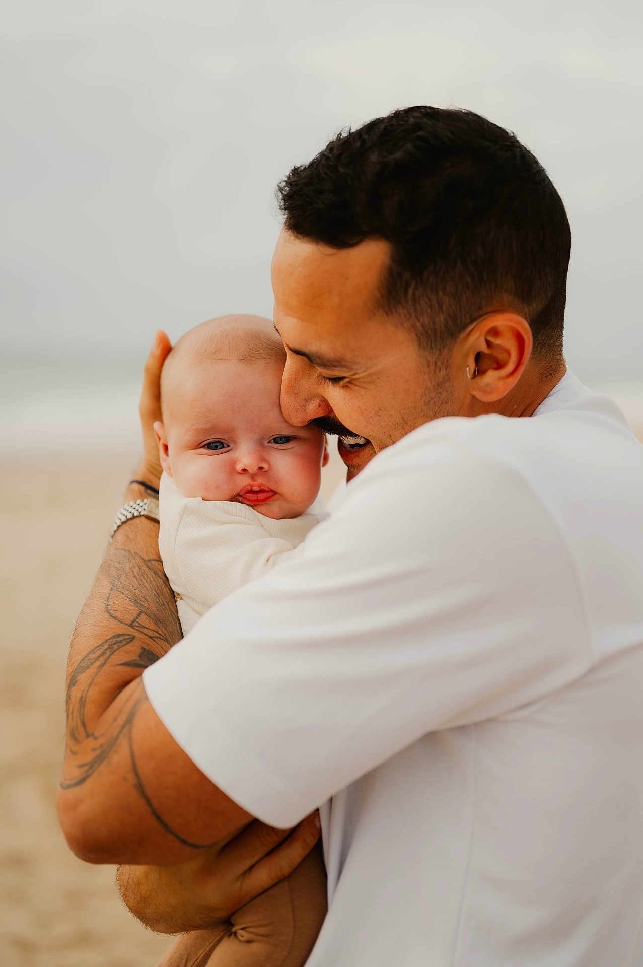 Raphaëlle participe au concours pour gagner de l'argent avec cette photo : baby, man, hug, tattoo, beach, smile, affection, love, outdoor, portrait, skin, white_shirt, closeup, father, child, person, casual_clothing, emotion, head, family
