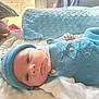 baby, infant, blue_knitwear, hat, blanket, white_clothing, indoor, natural_light, soft_texture, peaceful, lying_down, closeup, face, newborn, window, curtain, wooden_fence, cozy, buttoned_outfit, home