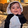 toddler, child, panda_onesie, smiling, cute, indoors, living_room, couch, blanket, hand_on_face, happy, portrait, cozy, baby, hoodie, furniture, expression, person, cute_outfit, home