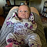 baby, infant, pajamas, person, face, legs, feet, socks, floral_pattern, living_room, television, bookshelf, photograph, furniture, indoors, curious, skin, expression, seated, cozy