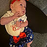 baby, infant, child, red_bow, headband, white_shirt, blue_skirt, stars, sitting, couch, cushion, barefoot, cute, portrait, indoor, clothing, person, hand, face, expression