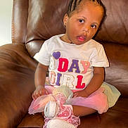 Elyse is registered to the contest to win money with this photo: child, girl, toddler, portrait, sitting, leather_couch, indoors, braids, hair_bows, earrings, white_shirt, colorful_clothing, skirt, sparkly_shoes, pink_shoes, fashion, serious_expression, face, furniture, home