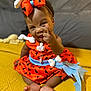 baby, child, smile, orange_dress, headband, bow, sitting, yellow_blanket, indoor, cute, happy, person, foot, hand, portrait, infant, clothing, playful, expression, fun