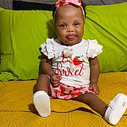 Elyse joined the competition — help win amazing prizes! baby, child, girl, sitting, smiling, headband, bow, strawberry, white_top, shorts, yellow_quilt, green_pillow, medical_device, indoors, cute, portrait, happy, clothing, person, feet
