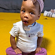 Elyse joined the competition — help win amazing prizes! toddler, child, baby, pink_bow, headband, sitting, yellow_background, purple_pants, white_shirt, text_on_shirt, love_my_family, cross_legged, indoor, curious_expression, white_socks, cute, face, person, small_ears, earrings
