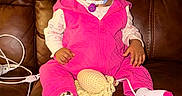 Elyse joined the competition — help win amazing prizes! brown_background, charging_cable, child, crochet_toy, cute, earring, feet, flash_lighting, hair_buns, hands, home, leather_couch, living_room, medical_tube, pink_outfit, plush_toy, portrait, sitting, socks, toddler