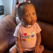 Elyse is registered to the contest to win money with this photo: toddler, child, braided_hair, pink_bows, pink_outfit, hearts, sitting, leather_chair, indoor, curious_expression, bandage, young_child, portrait, casual_clothing, cute, skin, face, hands, legs, home