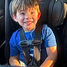 child, boy, car_seat, smile, blue_shirt, sunlight, seatbelt, car_interior, happy, young, portrait, sitting, face, hair, window, daylight, safety, casual_clothing, indoors, cute