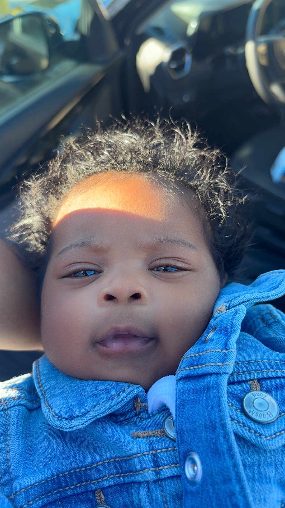 Kaylani is registered to the contest to win money with this photo: baby, child, face, denim_jacket, clothing, curly_hair, portrait, close_up, car_interior, seat, sunlight, shadow, cute, infant, young_child, skin, eyes, mouth, head, person