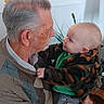 baby, cozy, elderly_man, face, gaze, grandparent, hands, holding, home, indoor, interaction, kitchen, love, patterned_jacket, person, plant, portrait, smile, sweater, vase