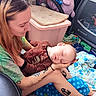 Atticus is registered to the contest to win money with this photo: adult, baby, blanket, casual_clothing, floor, holding, home_interior, infant, lap, nap, peaceful, playpen, portrait, sleeping, storage_bin, stroller, tattooed_arms, tattoos, toy, woman