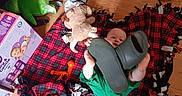 Atticus is registered to the contest to win money with this photo: baby, baby_bottle, blanket, cardboard_box, child, colorful_toy, elephant_plush, giraffe_toy, green_onesie, infant, pacifier, plaid_blanket, playroom, rattle, shoe, slipper, storage_bin, stuffed_animal, toy, wood_floor