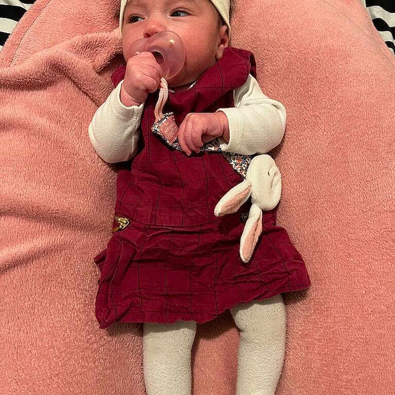 Aëla participe au concours pour gagner de l'argent avec cette photo : baby, bedding, blanket, bow, bunny, child, cozy, dress, face, hand, headband, infant, lying_down, maroon_dress, pacifier, pink_blanket, plush_toy, portrait, tights, white_sleeves