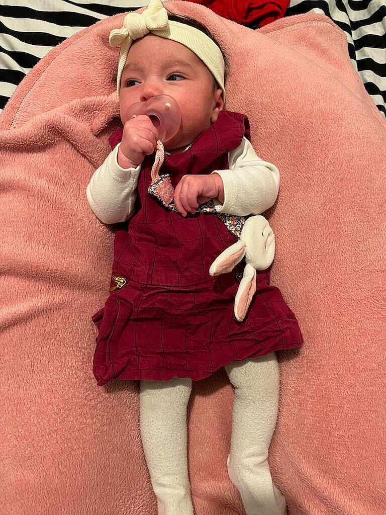 Aëla participe au concours pour gagner de l'argent avec cette photo : child, baby, infant, pacifier, headband, bow, blanket, pink_blanket, dress, maroon_dress, white_sleeves, tights, plush_toy, bunny, hand, face, portrait, lying_down, bedding, cozy