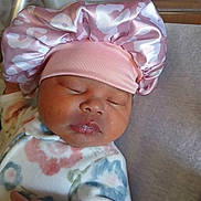 Zoē joined the competition — help win amazing prizes! baby, sleeping, infant, pink_bonnet, pajamas, floral_pattern, soft_fabric, close_up, face, peaceful, cute, resting, newborn, child, headwear, person, indoors, skin, hand, cozy