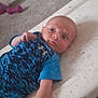 baby, infant, blue_clothing, onesie, lying_down, carpet, changing_pad, animal_print, hand, face, expression, indoor, toy, purple_toy, furniture, floor, person, newborn, child, cute