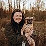 woman, dog, pug, outdoor, smiling, portrait, nature, trees, field, autumn, person, pet, animal, holding, casual_clothing, happy, brown, grass, sunlight, seasonal