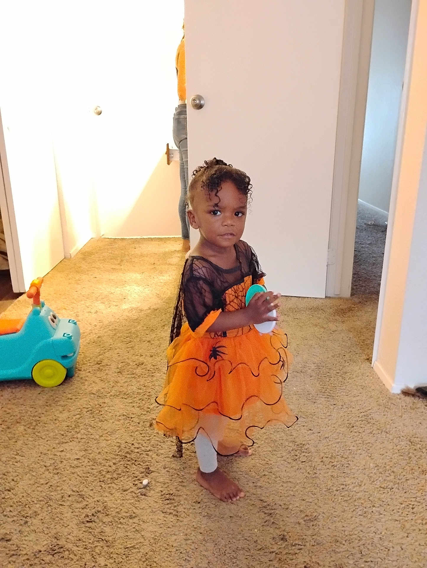 Aniya joined the competition — help win amazing prizes! child, toddler, dress, orange, black, carpet, indoor, toy, barefoot, person, curly_hair, hallway, door, adult, jeans, light, holding, floor, room, standing