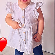 Victoire a rejoint le concours — aidez-le/la à gagner de superbes lots ! barefoot, buttoned_dress, child, cute, earring, foot, hair, happy, indoor, leggings, light_background, person, portrait, red_heart_emoji, small_child, smile, standing, toddler, white_dress, wooden_floor