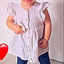barefoot, buttoned_dress, child, cute, earring, foot, hair, happy, indoor, leggings, light_background, person, portrait, red_heart_emoji, small_child, smile, standing, toddler, white_dress, wooden_floor