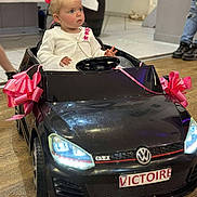 Victoire participe au concours pour gagner de l'argent avec cette photo : toddler, child, toy_car, volkswagen, indoor, pink_ribbon, floor, curious, white_jacket, steering_wheel, head, face, person, vehicle, small_car, flooring, event, decor, young_child, casual