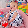 Victoire a rejoint le concours — aidez-le/la à gagner de superbes lots ! toddler, child, ball_pit, pink_balls, playpen, toys, red_bows, dress, smiling, indoor, play_area, colorful, happy, cute, baby, floor_mat, plastic_balls, childrens_room, face, earrings