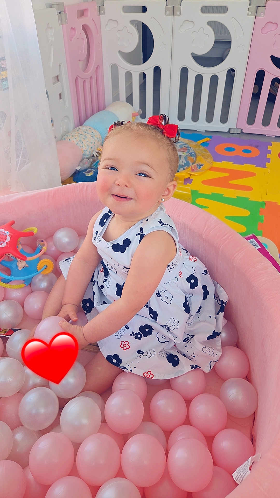 Victoire a rejoint le concours — aidez-le/la à gagner de superbes lots ! toddler, child, ball_pit, pink_balls, playpen, toys, red_bows, dress, smiling, indoor, play_area, colorful, happy, cute, baby, floor_mat, plastic_balls, childrens_room, face, earrings