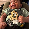 baby, car_seat, cartoon, child, close_up, clothing, curly_hair, face, green_shirt, hands, happy, indoor, infant, mickey_mouse, passenger, photography, portrait, seated, smiling, vehicle