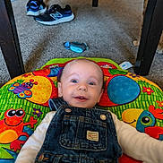 Ryan joined the competition — help win amazing prizes! baby, denim_overalls, play_mat, colorful, carpet, floor, sneakers, cat, table, indoor, smiling, child, face, clothing, infant, cute, happy, toy, person, casual