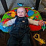 Ryan is registered to the contest to win money with this photo: baby, child, denim_overalls, colorful_pillow, toy, carpet, floor, indoor, playtime, smiling, motion_blur, pet, animal, giraffe_toy, happy, infant, person, cute, blue, casual_clothing
