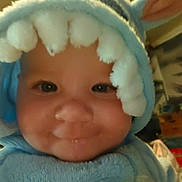 Hylda a rejoint le concours — aidez-le/la à gagner de superbes lots ! baby, child, costume, blue, bunny_ears, pom_poms, face, smile, indoor, close_up, cute, soft_texture, hood, apparel, person, infant, portrait, warm_lighting, adorable, expression