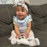 Journeylynn is registered to the contest to win money with this photo: baby, child, girl, couch, controller, headband, smile, sitting, sock, clothing, curly_hair, indoor, person, cute, happy, game_controller, fabric, pattern, home, light
