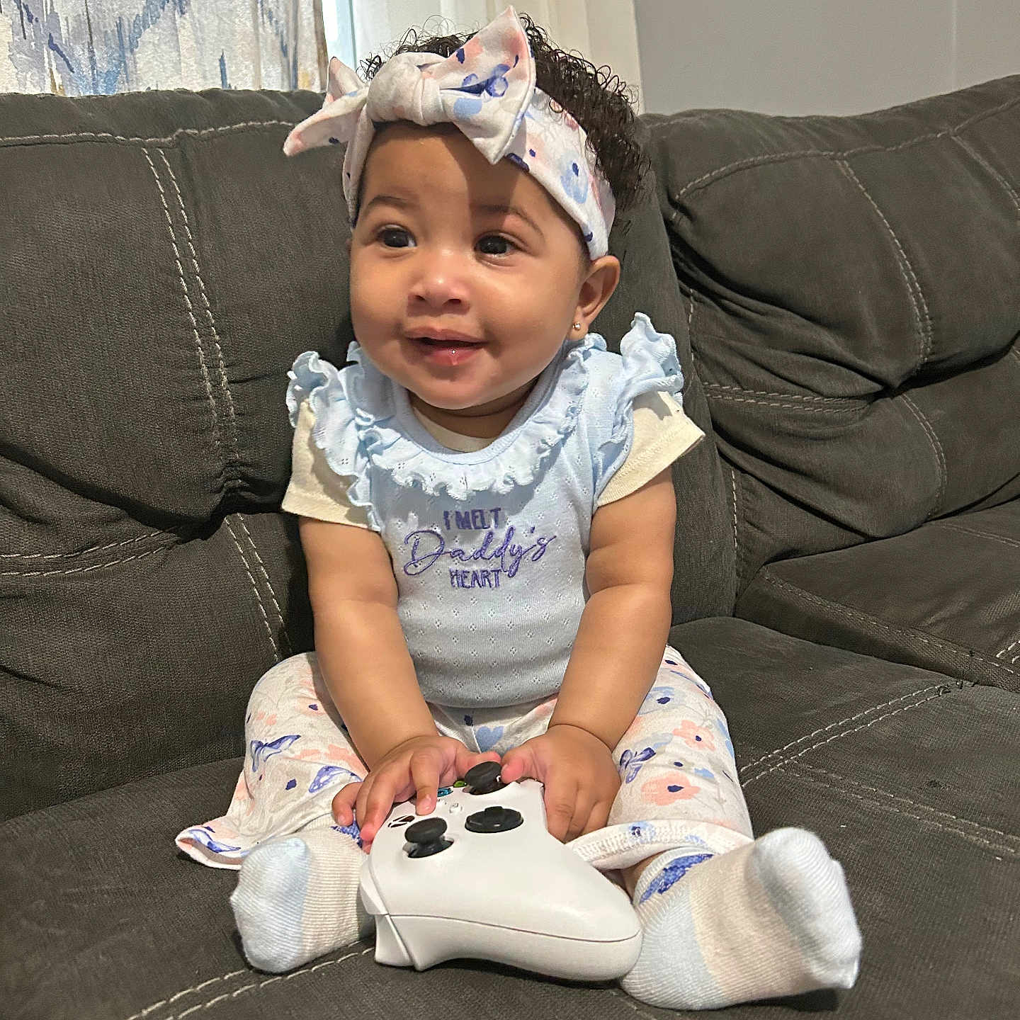 Journeylynn is registered to the contest to win money with this photo: baby, child, clothing, controller, couch, curly_hair, cute, fabric, game_controller, girl, happy, headband, home, indoor, light, pattern, person, sitting, smile, sock