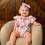 baby, child, infant, girl, smile, headband, bow, floral_outfit, chair, furniture, wooden_background, portrait, indoors, cute, happy, seated, skin, legs, hands, eyes