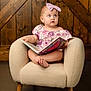 baby, child, girl, bow, headband, book, reading, armchair, furniture, wooden_background, indoors, cute, curious, portrait, infant, pink, purple, floral_dress, barefoot, sitting