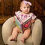 baby, child, girl, reading, book, armchair, headband, pink_bow, blue_eyes, wooden_background, cozy, indoor, portrait, cute, curious, soft_lighting, clothing, sitting, infant, expression