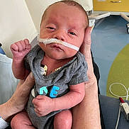 Grayson joined the competition — help win amazing prizes! newborn, baby, infant, hospital, medical_tube, nasal_cannula, onesie, tattoo, hand, arm, person, indoor, medical_equipment, hospital_room, patient, resting, closeup, skin, healthcare, care