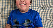 Grayson is registered to the contest to win money with this photo: blanket, blue_shirt, casual_clothing, child, chubby_cheeks, couch, hand, happy, holding_shoe, indoor, living_room, plaid_couch, portrait, seated, short_hair, smiling, sneaker, teeth, toddler, under_armour_logo