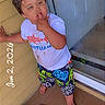 Grayson is registered to the contest to win money with this photo: toddler, child, barefoot, porch, door, stickers, white_tshirt, colorful_shorts, finger_in_mouth, curious, standing, floor_mat, outdoor, hand_on_wall, messy, playful, young_child, casual, daylight, person