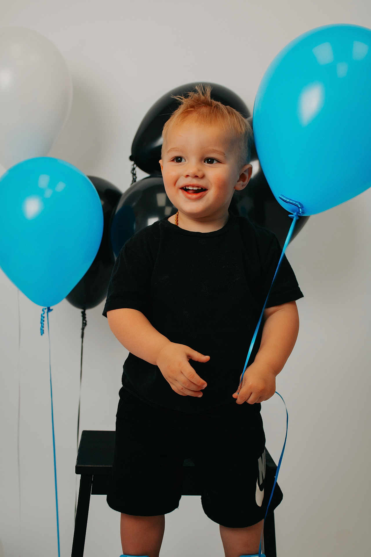 Kendrix is registered to the contest to win money with this photo: child, toddler, balloon, blue_balloon, black_balloon, white_balloon, smiling, happy, standing, shorts, tshirt, indoor, party, celebration, cute, young_child, hair, holding, person, studio