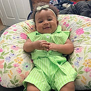 Nariah is registered to the contest to win money with this photo: baby, bedroom, bow, child, cozy, curly_hair, dresser, floral_pillow, furniture, green_outfit, hands, headband, home, indoors, infant, lying_down, photograph, portrait, sitting, smiling