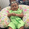 baby, child, infant, smiling, portrait, indoors, green_outfit, headband, bow, floral_pillow, bedroom, dresser, furniture, lying_down, sitting, hands, curly_hair, cozy, home, photograph