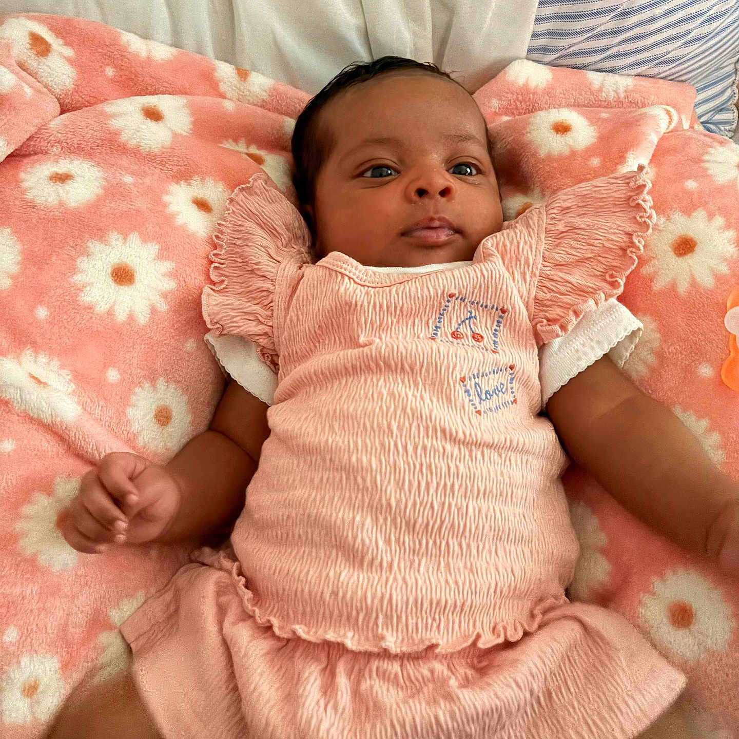 Amora is registered to the contest to win money with this photo: baby, infant, child, pink_clothing, blanket, floral_pattern, cute, lying_down, portrait, soft_texture, indoors, cozy, comfortable, small_hands, smiling, young_child, head, face, skin, happy