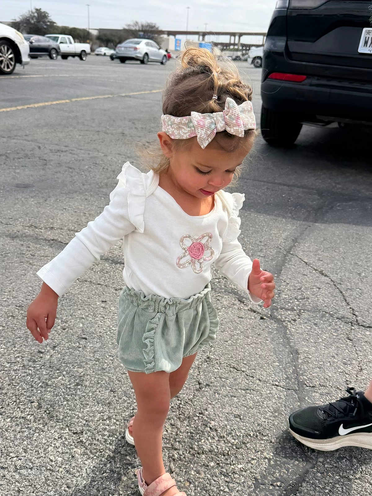Kiana joined the competition — help win amazing prizes! child, toddler, girl, headband, bow, white_shirt, ruffle_shorts, green_shorts, sandals, parking_lot, pavement, car, suv, walking, cute, outdoor, candid, hair, smile, adult_shoe